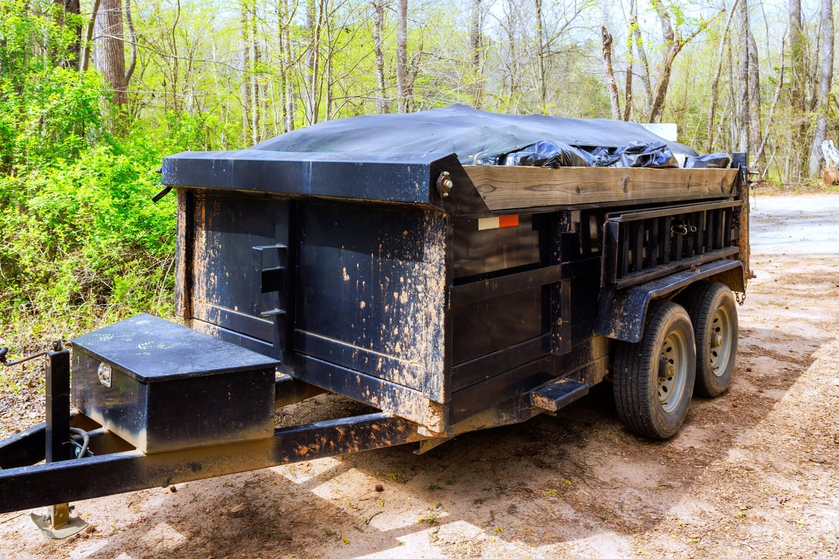 Dumpster trailer beside a rural dirt road near trees